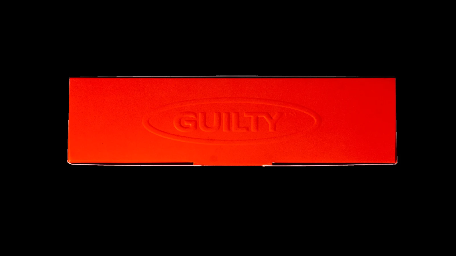 Top-down close-up of The First Offence box detail — embossed GUILTY oval wordmark on Guilty Orange card stock, debossed print finish.